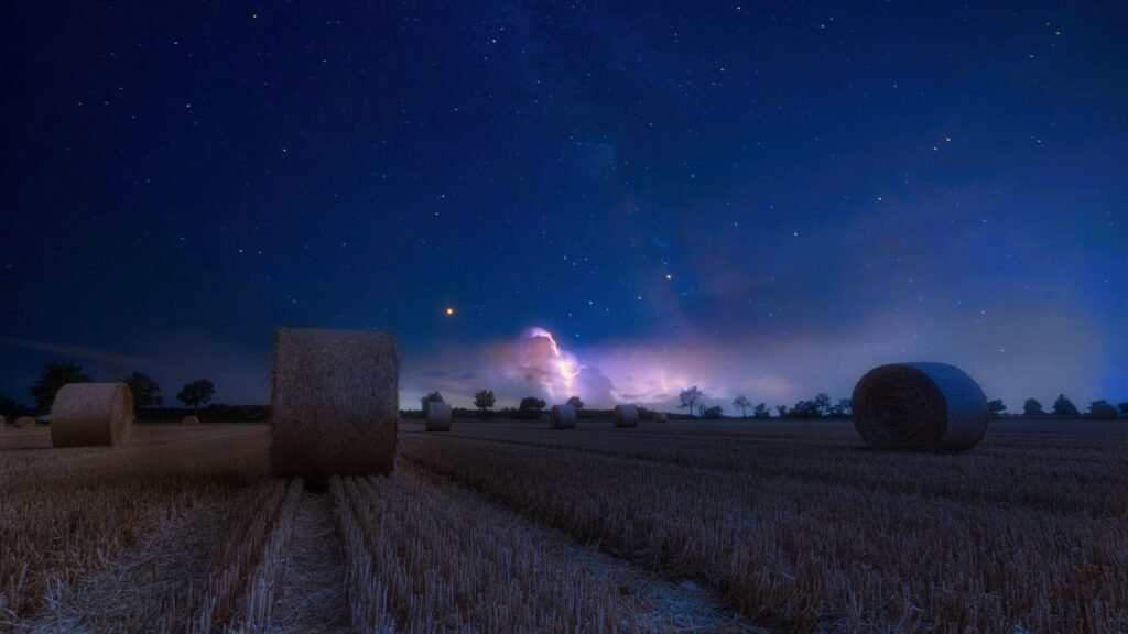 A scenic rural landscape featuring hay bales under a starry night sky, perfect for serene and dreamy nature themes.